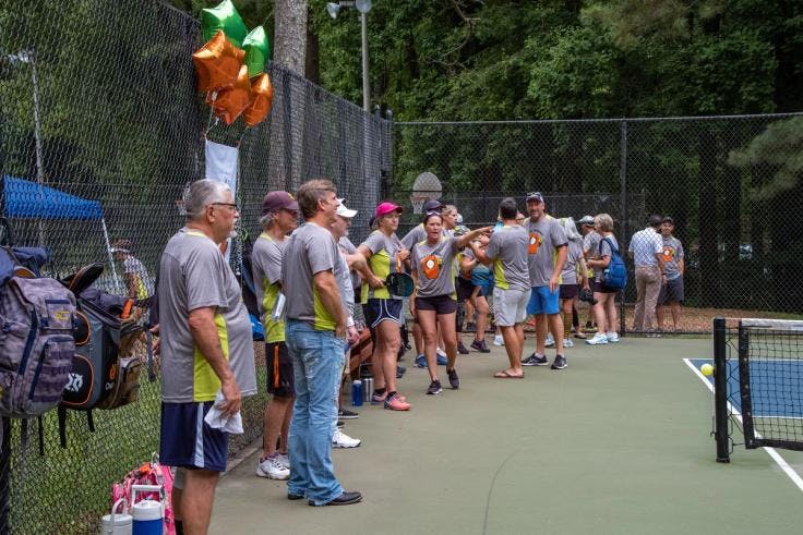 Players stand at the side of a pickleball court during an open play session